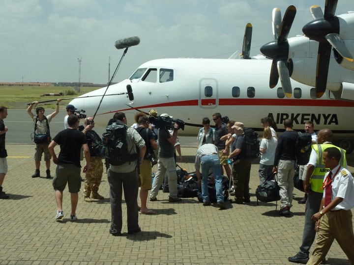 Film crew unloading equipment beside an Air Kenya plane